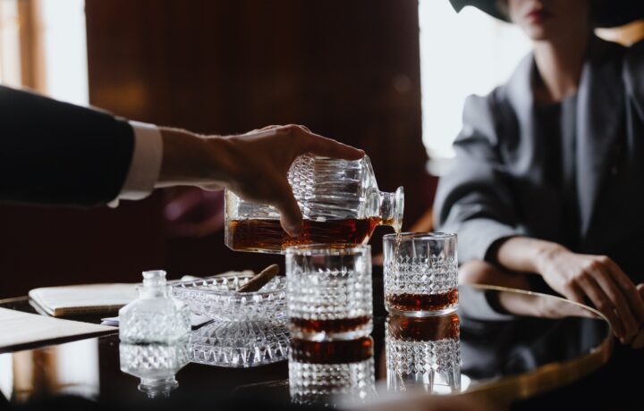 Person pouring cognac into two crystal glasses.